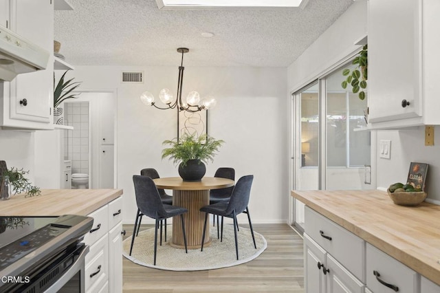 dining space with a textured ceiling, light hardwood / wood-style floors, and a notable chandelier