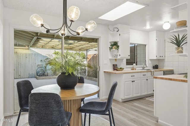 dining area featuring an inviting chandelier, a skylight, sink, and light hardwood / wood-style flooring