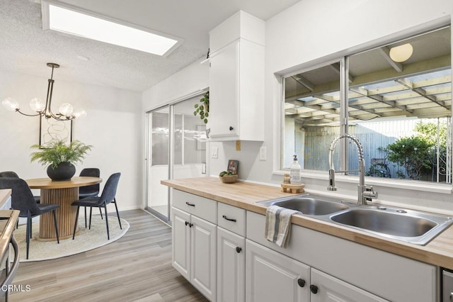 kitchen with sink, wooden counters, decorative light fixtures, white cabinets, and light wood-type flooring