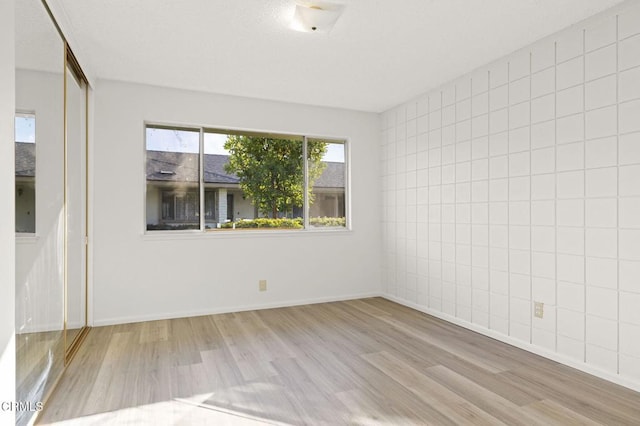 unfurnished room with light wood-type flooring and tile walls