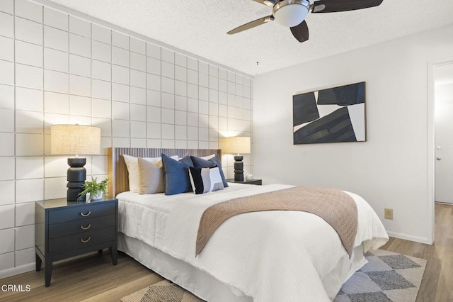 bedroom with a textured ceiling, light hardwood / wood-style floors, tile walls, and ceiling fan