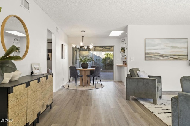 interior space with a notable chandelier, a skylight, a textured ceiling, and light hardwood / wood-style flooring