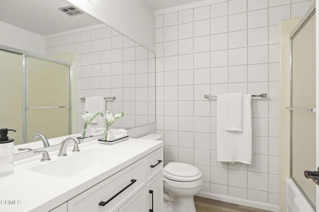 full bathroom with combined bath / shower with glass door, vanity, hardwood / wood-style flooring, tile walls, and toilet