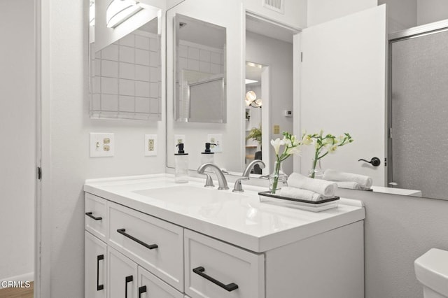 bathroom featuring a shower with door, vanity, and toilet