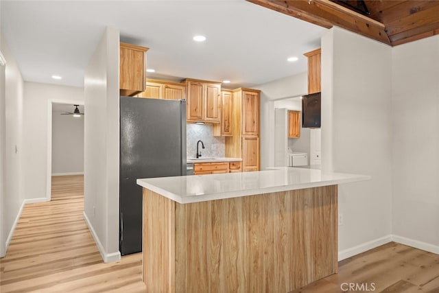 kitchen with stainless steel fridge, backsplash, sink, light hardwood / wood-style flooring, and washing machine and dryer