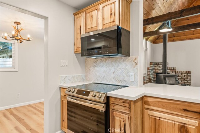 kitchen featuring decorative backsplash, stainless steel appliances, light hardwood / wood-style flooring, a notable chandelier, and a wood stove