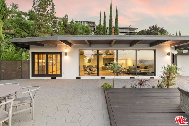 back house at dusk featuring a deck and a patio