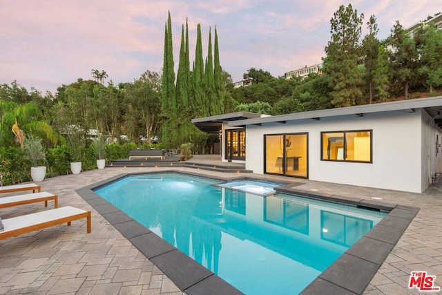 pool at dusk featuring an in ground hot tub and a patio