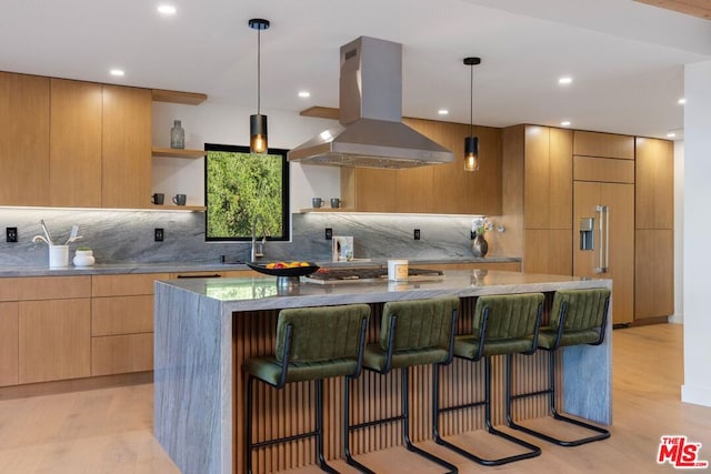 kitchen featuring a kitchen breakfast bar, tasteful backsplash, island range hood, light hardwood / wood-style flooring, and hanging light fixtures