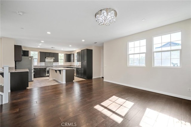 kitchen featuring dark wood-type flooring, stainless steel refrigerator, a kitchen bar, tasteful backsplash, and a kitchen island