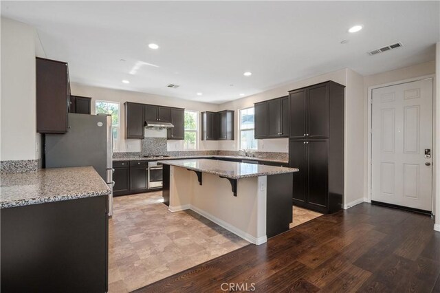 kitchen featuring a kitchen bar, a kitchen island, stainless steel appliances, light stone countertops, and hardwood / wood-style floors