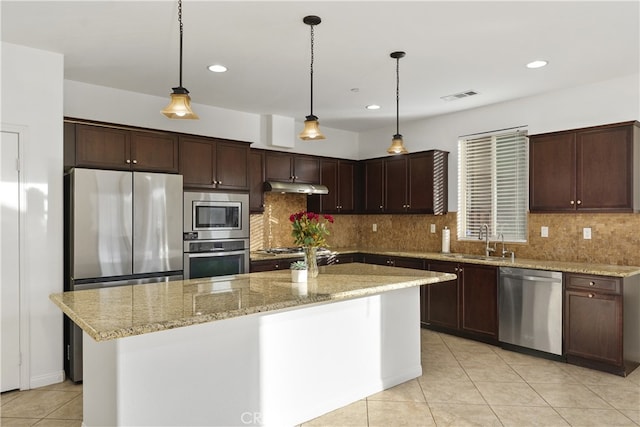 kitchen with a center island, sink, stainless steel appliances, light stone counters, and pendant lighting