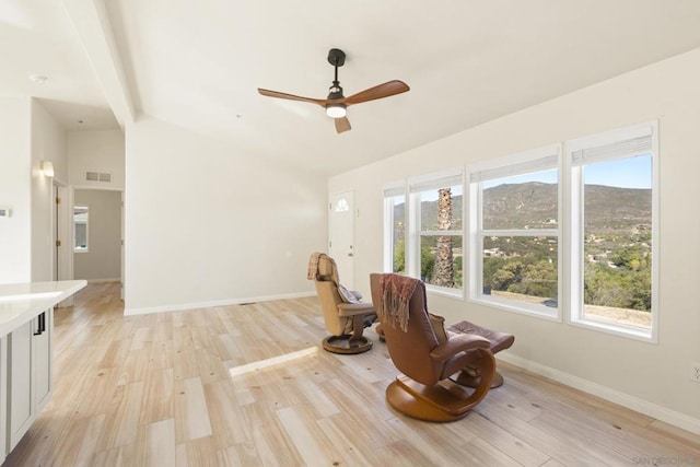 unfurnished room featuring a mountain view, light wood-type flooring, vaulted ceiling, and ceiling fan