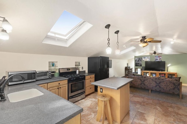 kitchen featuring appliances with stainless steel finishes, vaulted ceiling with skylight, ceiling fan, sink, and a kitchen island