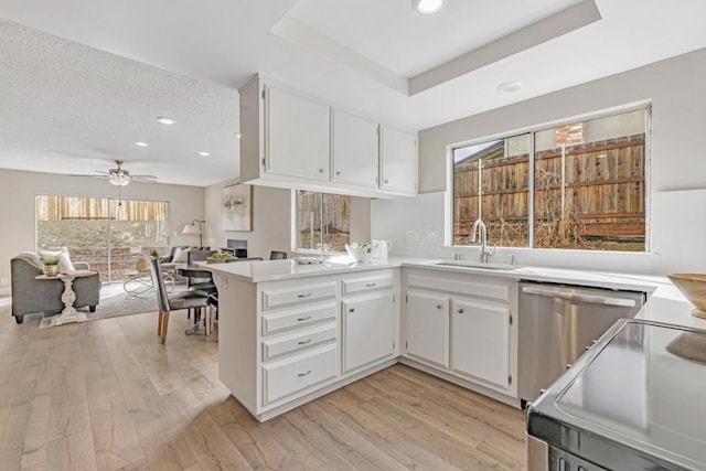 kitchen featuring sink, a tray ceiling, white cabinets, stainless steel dishwasher, and kitchen peninsula