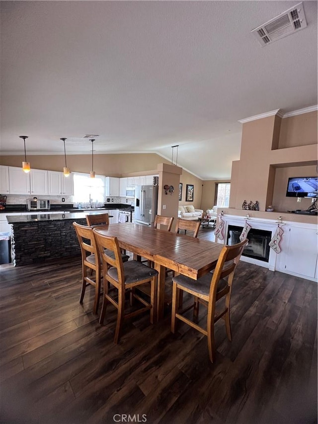 dining room featuring plenty of natural light, dark hardwood / wood-style flooring, ornamental molding, and vaulted ceiling