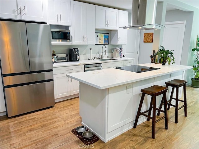 kitchen featuring wall chimney exhaust hood, stainless steel appliances, a kitchen island, light hardwood / wood-style flooring, and white cabinets