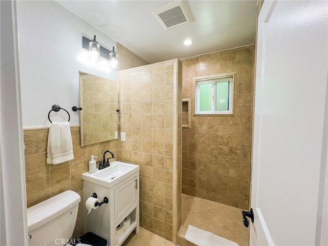 bathroom featuring tile patterned flooring, toilet, tiled shower, vanity, and tile walls