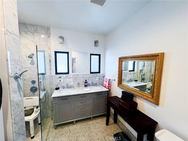 bathroom featuring tasteful backsplash, tile patterned flooring, toilet, tiled shower, and vanity