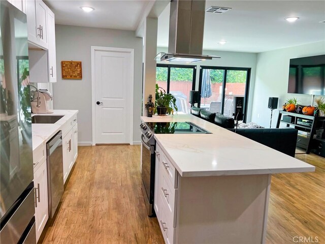 kitchen featuring light hardwood / wood-style flooring, light stone countertops, island range hood, white cabinetry, and stainless steel appliances