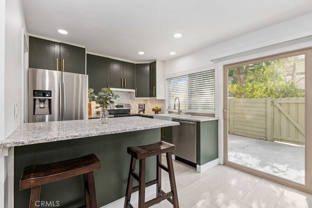 kitchen with a kitchen bar, sink, tasteful backsplash, light stone counters, and stainless steel appliances