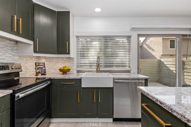 kitchen featuring sink, light stone counters, decorative backsplash, appliances with stainless steel finishes, and green cabinetry