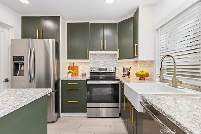 kitchen featuring light stone countertops, appliances with stainless steel finishes, green cabinetry, and sink