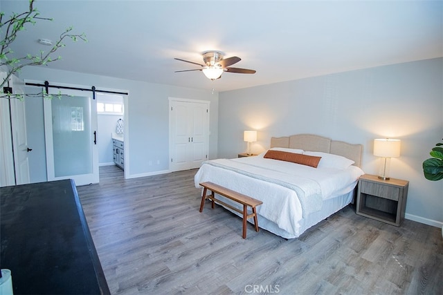 bedroom with connected bathroom, ceiling fan, a barn door, hardwood / wood-style floors, and a closet