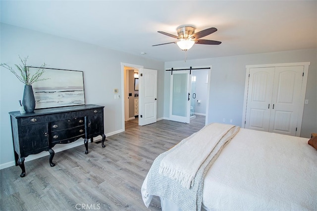 bedroom with wood-type flooring, a barn door, ensuite bath, and ceiling fan