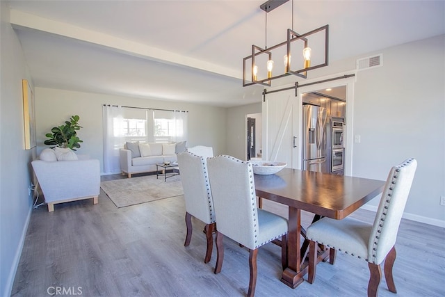 dining area with a barn door, hardwood / wood-style flooring, and a notable chandelier