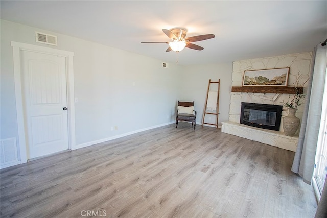 unfurnished room with light hardwood / wood-style flooring, ceiling fan, and a stone fireplace