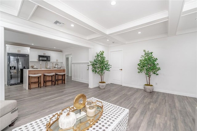 living room with coffered ceiling, sink, crown molding, light wood-type flooring, and beamed ceiling