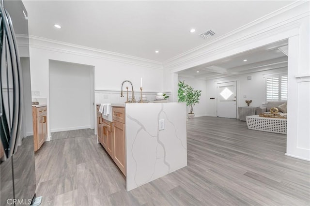 kitchen with light brown cabinetry, crown molding, fridge, and light hardwood / wood-style floors