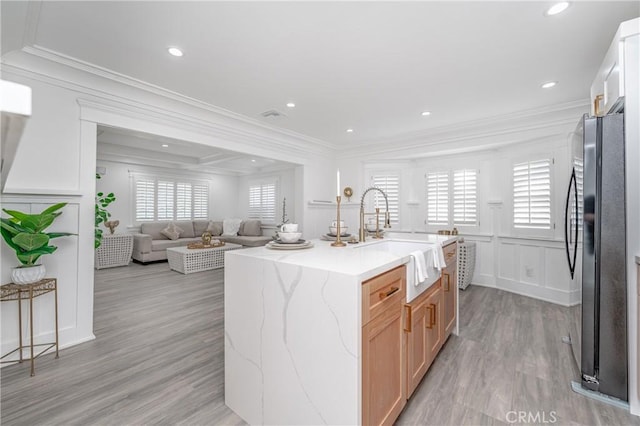 kitchen featuring sink, crown molding, light brown cabinets, black refrigerator, and an island with sink