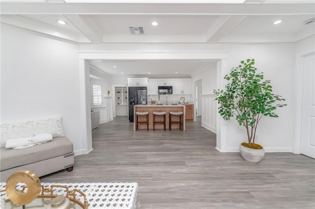 living room featuring beam ceiling, ornamental molding, and light wood-type flooring