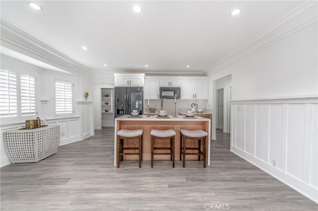 kitchen featuring white cabinets, a kitchen breakfast bar, black appliances, crown molding, and a center island with sink