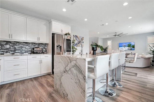 kitchen with plenty of natural light, stainless steel refrigerator with ice dispenser, light stone countertops, an island with sink, and white cabinets