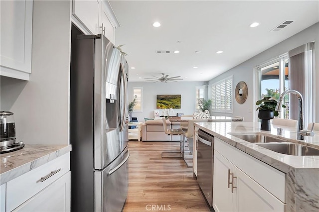 kitchen with sink, light hardwood / wood-style flooring, appliances with stainless steel finishes, white cabinetry, and light stone counters