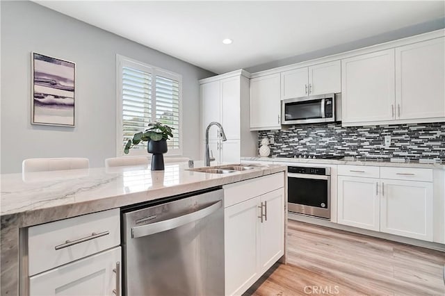 kitchen with light stone counters, appliances with stainless steel finishes, sink, and white cabinets