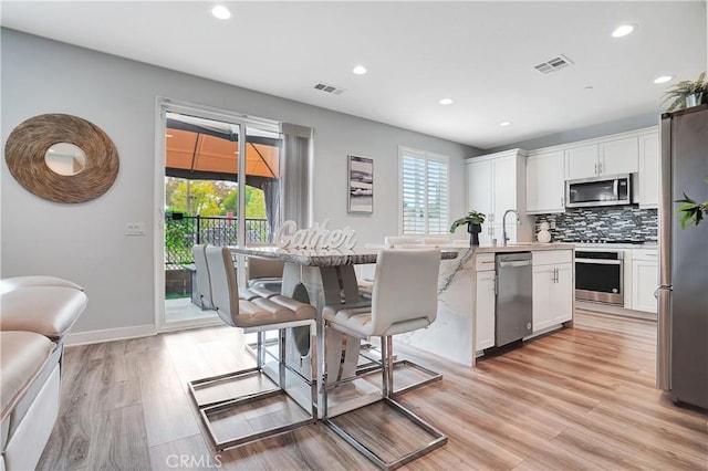 kitchen featuring appliances with stainless steel finishes, a kitchen breakfast bar, a healthy amount of sunlight, white cabinets, and decorative backsplash