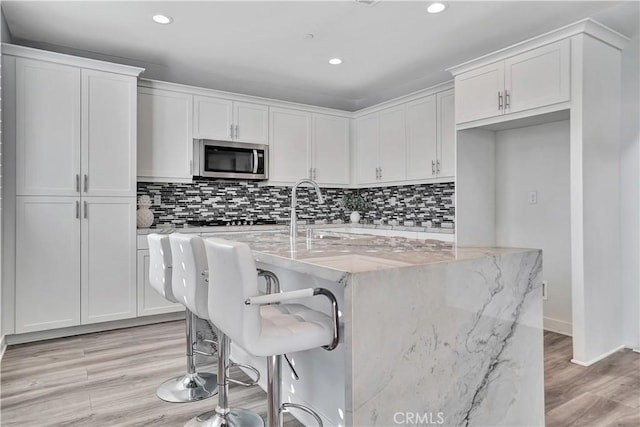 kitchen featuring a kitchen breakfast bar, an island with sink, white cabinets, and light stone counters