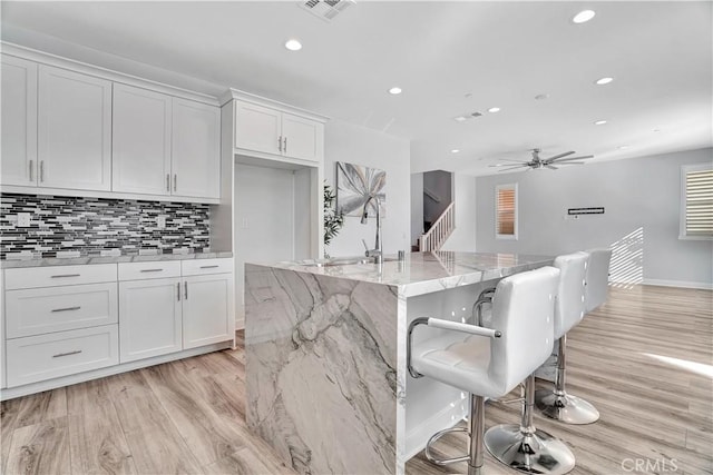 kitchen with light stone countertops, a breakfast bar area, a center island with sink, and white cabinets