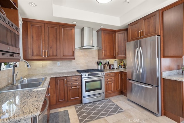 kitchen featuring light stone countertops, appliances with stainless steel finishes, sink, and wall chimney range hood