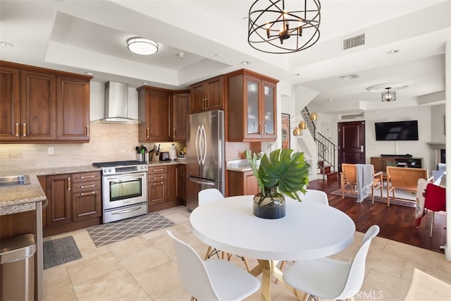 kitchen featuring pendant lighting, stainless steel appliances, a raised ceiling, and wall chimney range hood