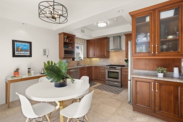 kitchen with light stone counters, wall chimney range hood, hanging light fixtures, and stainless steel appliances