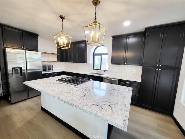 kitchen with tasteful backsplash, appliances with stainless steel finishes, pendant lighting, a kitchen island, and light wood-type flooring