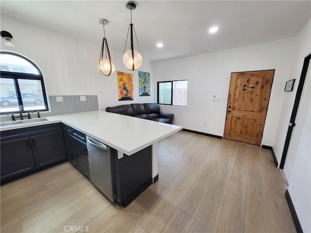 kitchen with kitchen peninsula, sink, decorative light fixtures, dishwasher, and light hardwood / wood-style floors