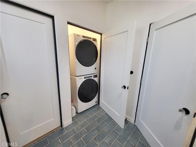 laundry area with stacked washing maching and dryer and dark tile patterned flooring