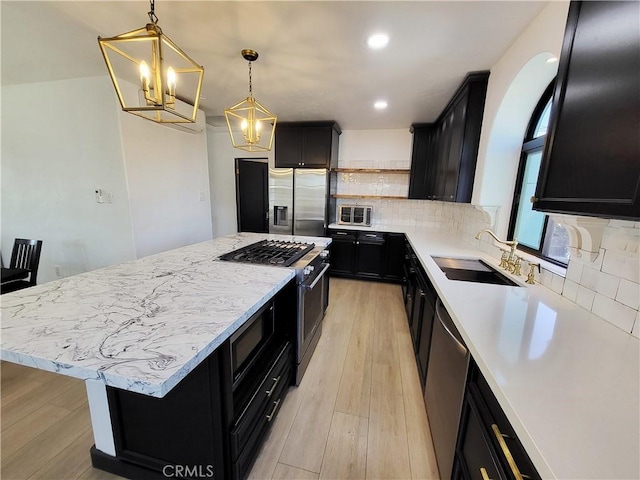 kitchen with appliances with stainless steel finishes, sink, decorative light fixtures, light hardwood / wood-style floors, and a kitchen island