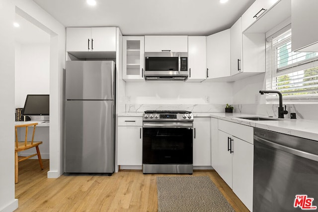 kitchen featuring light stone countertops, white cabinetry, sink, light hardwood / wood-style floors, and appliances with stainless steel finishes